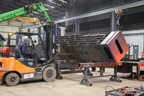 Steel structure being lifted by a crane with a fork truck in front