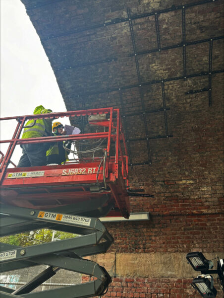 Image of workers in a scissor lift under a brick bridge