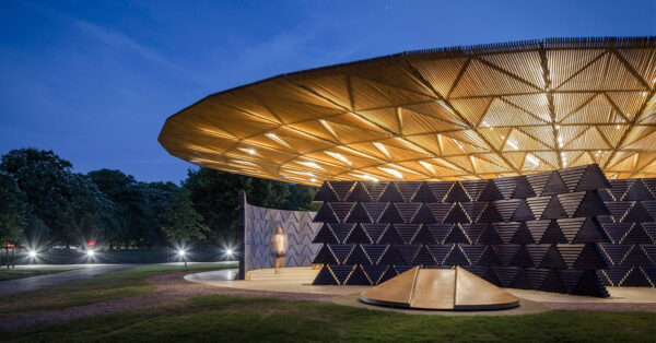 Image of Serpentine Pavilion 2017 designed by Francis Kéré, blue component walls with overhead timber canopy, seen at dusk